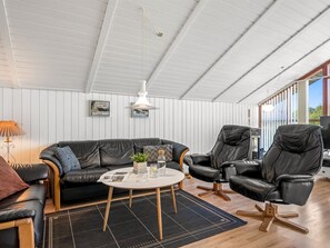 A modern living room with a black leather sofa, a round coffee table, and a black leather armchair. There is a white ceiling with wooden beams, a hanging pendant light, and a window providing natural light. - "Aida" - 550m from the sea by Interhome (Esbjerg V)