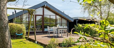 Una casa moderna con un invernadero de vidrio, una terraza de madera y un comedor.