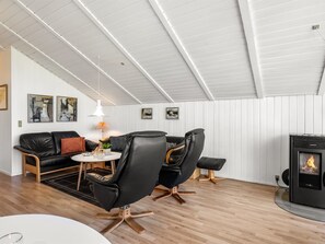Ein modernes Wohnzimmer mit einer schwarzen Ledersofa, einem runden Couchtisch und einem schwarzen Ledersessel. Es gibt einen kleinen runden Tisch mit einer Lampe, einen schwarzen Hocker und einen Kaminofen.