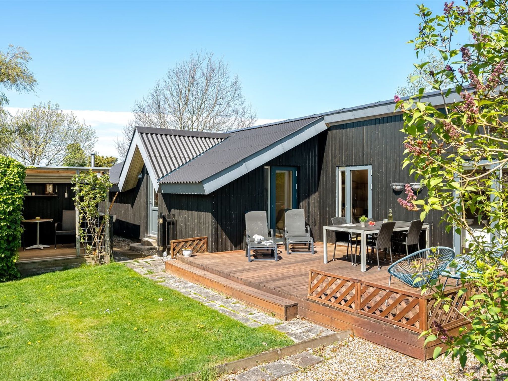 Ein modernes Haus mit Terrasse, Sitzgelegenheit im Freien und einem Garten.