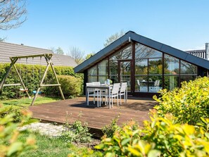 Ein modernes Haus mit einer Terrasse, einer Schaukel und einem Essbereich mit Gartenmöbeln.