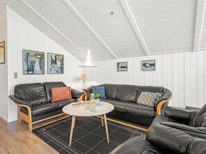 Ein modernes Wohnzimmer mit einem schwarzen Ledersofa, einem runden Couchtisch und einer hängenden Pendelleuchte.
