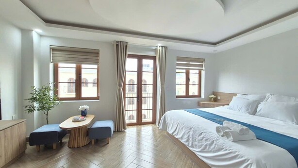 A hotel room with a bed, a dining table, two chairs, a small plant, and a view of the outside through a window. - LANA SEA (An Thoi)