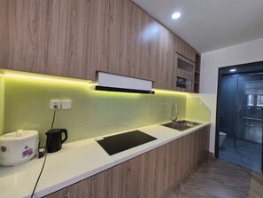 Eine moderne Küche mit weißer Arbeitsplatte, Holzschränken, einem schwarzen Wasserkocher und einem weißen Gerät mit violetten Blumen.