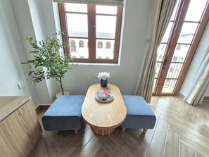 Ein Essbereich mit einem Holztisch, zwei blauen Sitzbänken, einer Topfpflanze und einem Fenster mit Blick auf Gebäude.