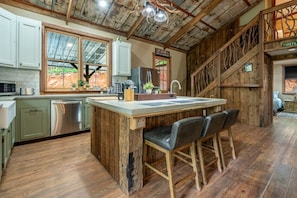 A rustic kitchen with a wooden island, bar stools, and a view of the outdoors.