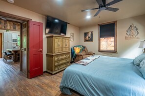 A bedroom with a bed, a television, a red door, a wooden cabinet, and a window.