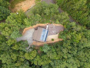 An aerial view of a building surrounded by dense forest, with a clear road leading to it.