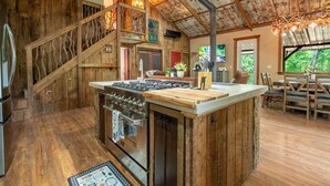 A rustic kitchen with a central island, wooden flooring, and a staircase leading to an upper level. - Firefly Retreat - Upscale Off-Grid Mountain Cabin (Marble Hill)