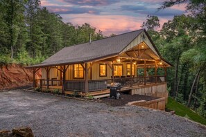 A cabin with a covered porch, a grill outside, and a view of the surrounding forest.