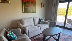 Ein Wohnzimmer mit einer Couch, einem Sessel und einem runden Couchtisch. Auf dem Boden liegt ein gemustertes Teppich.