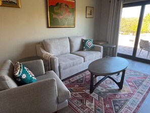 Ein Wohnzimmer mit einer Couch, einem Sessel und einem runden Couchtisch. Auf dem Boden liegt ein gemustertes Teppich.