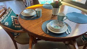 Ein runder Holztisch mit blauer Tischmatte, einer dekorativen Schale, einer Tasse und einem kleinen Topfpflanz.