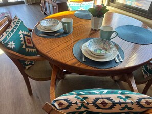 Ein runder Holztisch mit blauer Tischmatte, einer dekorativen Schale, einer Tasse und einem kleinen Topfpflanz.