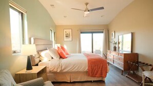 Ein Schlafzimmer mit einem Bett, Nachttischen, einem Sessel, einer Kommode und einem Deckenventilator.