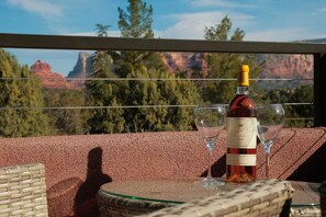 Una botella de vino y dos copas sobre una mesa, con una vista panorámica de montañas al fondo.