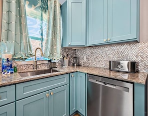 A kitchen with teal cabinets, a stainless steel dishwasher, and a toaster. - Blue Lagoon • New Villa Near Beach (Galveston)