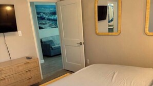 Un dormitorio con cama, cómoda, televisor y puerta que da a otra habitación.