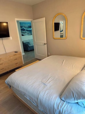 A bedroom with a bed, a dresser, a television, and a door leading to another room. - Blue Lagoon • New Villa Near Beach (Galveston)