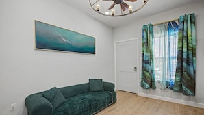 Una stanza con un divano verde, una ventola a soffitto, un quadro e una porta con tende.