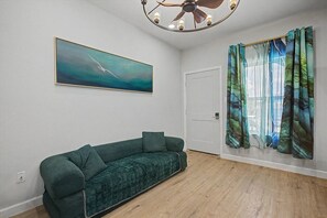 Ein Zimmer mit einem grünen Sofa, einem Deckenventilator, einem Gemälde und einer mit Vorhängen versehenen Tür.