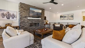 A modern living room with a stone fireplace, a ceiling fan, and a mounted TV. - Mountain Haus, Hot Tub, Sauna, Deer Valley Close (Heber City)