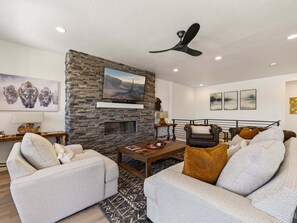 A modern living room with a stone fireplace, a ceiling fan, and a mounted TV. - Mountain Haus, Hot Tub, Sauna, Deer Valley Close (Heber City)