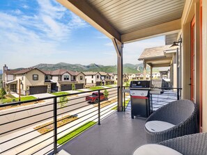 A covered balcony with a grill and wicker furniture, overlooking a street with houses and mountains. - Mountain Haus, Hot Tub, Sauna, Deer Valley Close (Heber City)