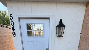 A white door with a number '5049' on the wall, a black lantern, and a white bench.