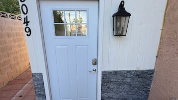 A white door with a number '5049' on the wall, a black lantern, and a white bench.