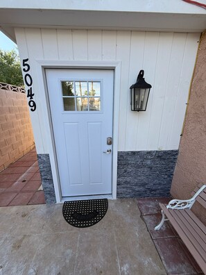 A white door with a number '5049' on the wall, a black lantern, and a white bench.