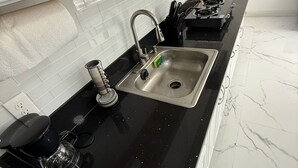 A kitchen with a black countertop, stainless steel sink, and white cabinets.