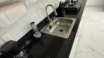 A kitchen with a black countertop, stainless steel sink, and white cabinets.