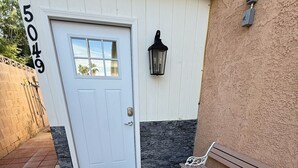 A house entrance with a white door, a mailbox, a bench, and a wall-mounted light fixture.