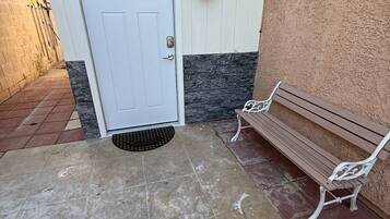 A house entrance with a white door, a mailbox, a bench, and a wall-mounted light fixture.