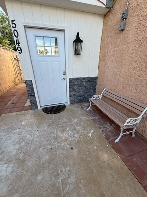 A house entrance with a white door, a mailbox, a bench, and a wall-mounted light fixture.