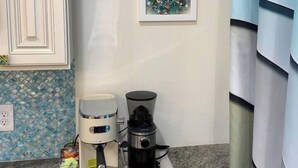 Uma bancada de cozinha com uma cafeteira, uma chaleira e uma caixa de cápsulas de café.