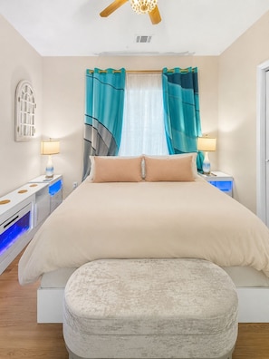 Ein Schlafzimmer mit einem Bett, zwei Nachttischen, einem Fenster mit Vorhängen und einem Deckenventilator.