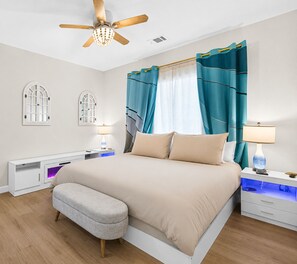 Ein modernes Schlafzimmer mit Bett, Nachttischen, Schreibtisch, Deckenventilator und einem Fenster mit Vorhängen.