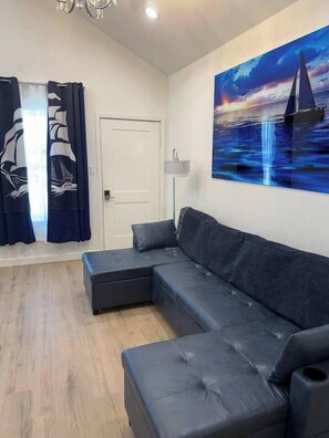 Un salon moderne avec un canapé d’angle, une porte et un grand tableau représentant un voilier accroché au mur.