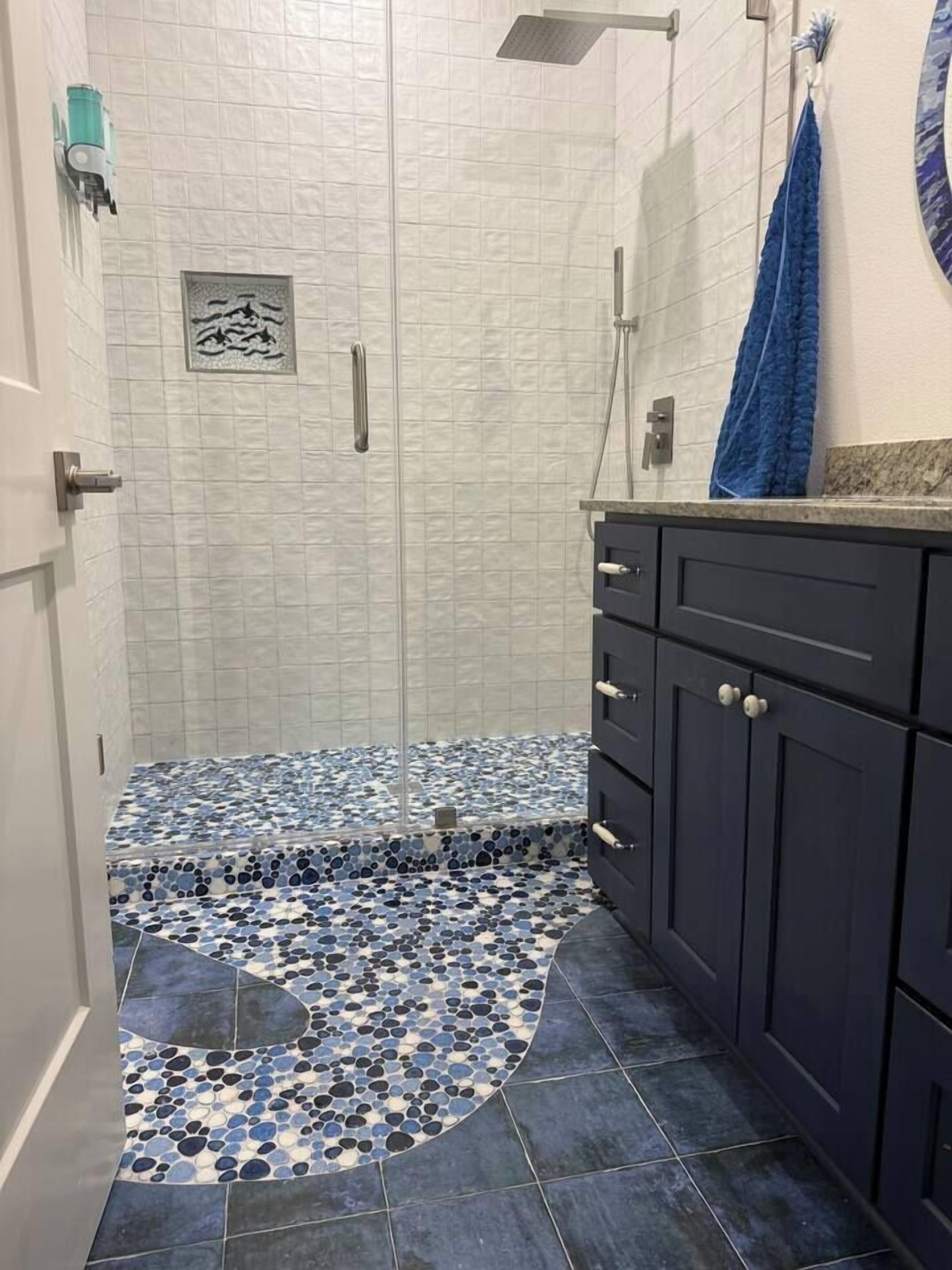 A bathroom with a shower area, tiled floor, and dark cabinets.