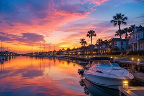 A marina at sunset with boats docked, waterfront houses, and palm trees. - Twilight Harbor • New Villa Near Beach (Galveston)