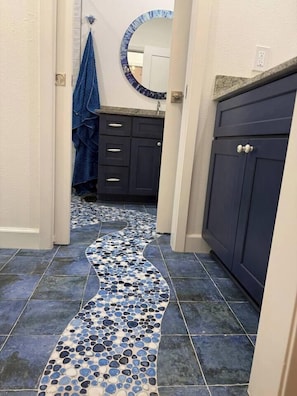 A bathroom with dark cabinets, a blue towel, and a tiled floor with a blue and white pattern. - Twilight Harbor • New Luxury Beach Villa•Sleeps 5 (Galveston)