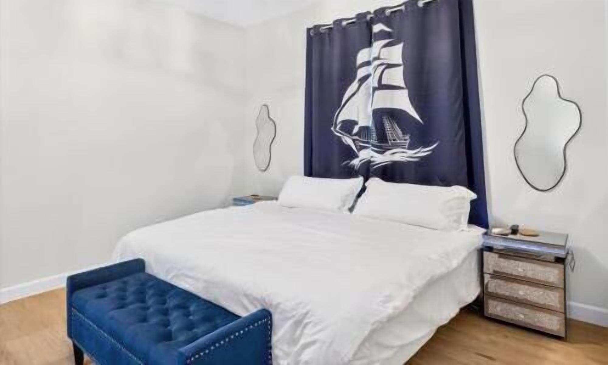 Een slaapkamer met een bed, een blauwe gestoffeerde bank, een nachtkastje en een muur met een ontwerp van een zeilboot.