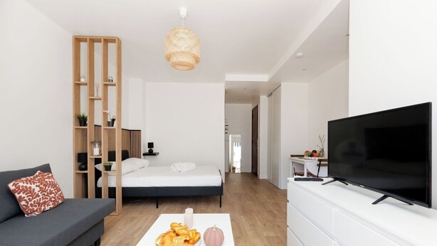 Uma sala de estar moderna com sofá, cama, televisão e área de jantar com mesa e cadeiras.