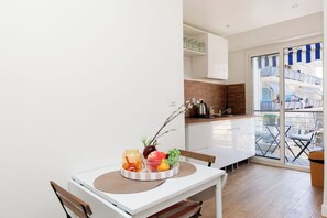 A modern kitchen with white cabinets, a wooden countertop, and a view of a balcony with outdoor furniture. - Upstays Studio 28m2 Balcony AC (Cannes)