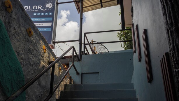 Una escalera conduce a la entrada de un hotel, con un cartel que indica servicios como habitaciones privadas y un bar salón.