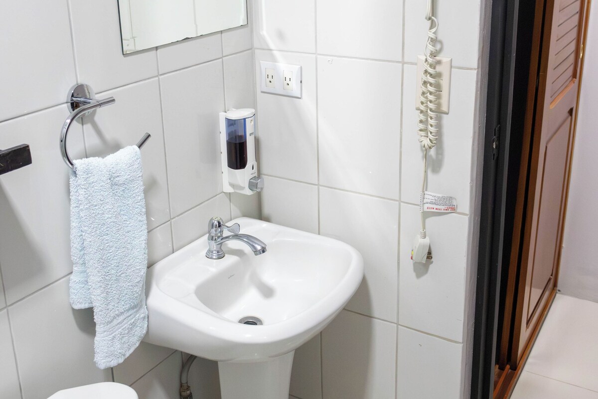 Un baño con lavamanos blanco, espejo, toallero y secador de pelo.