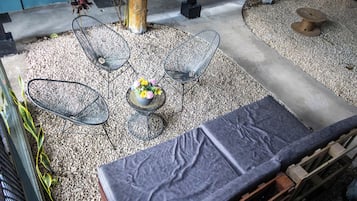 Un patio con sillas metálicas, una mesa con un arreglo floral y un sofá gris.