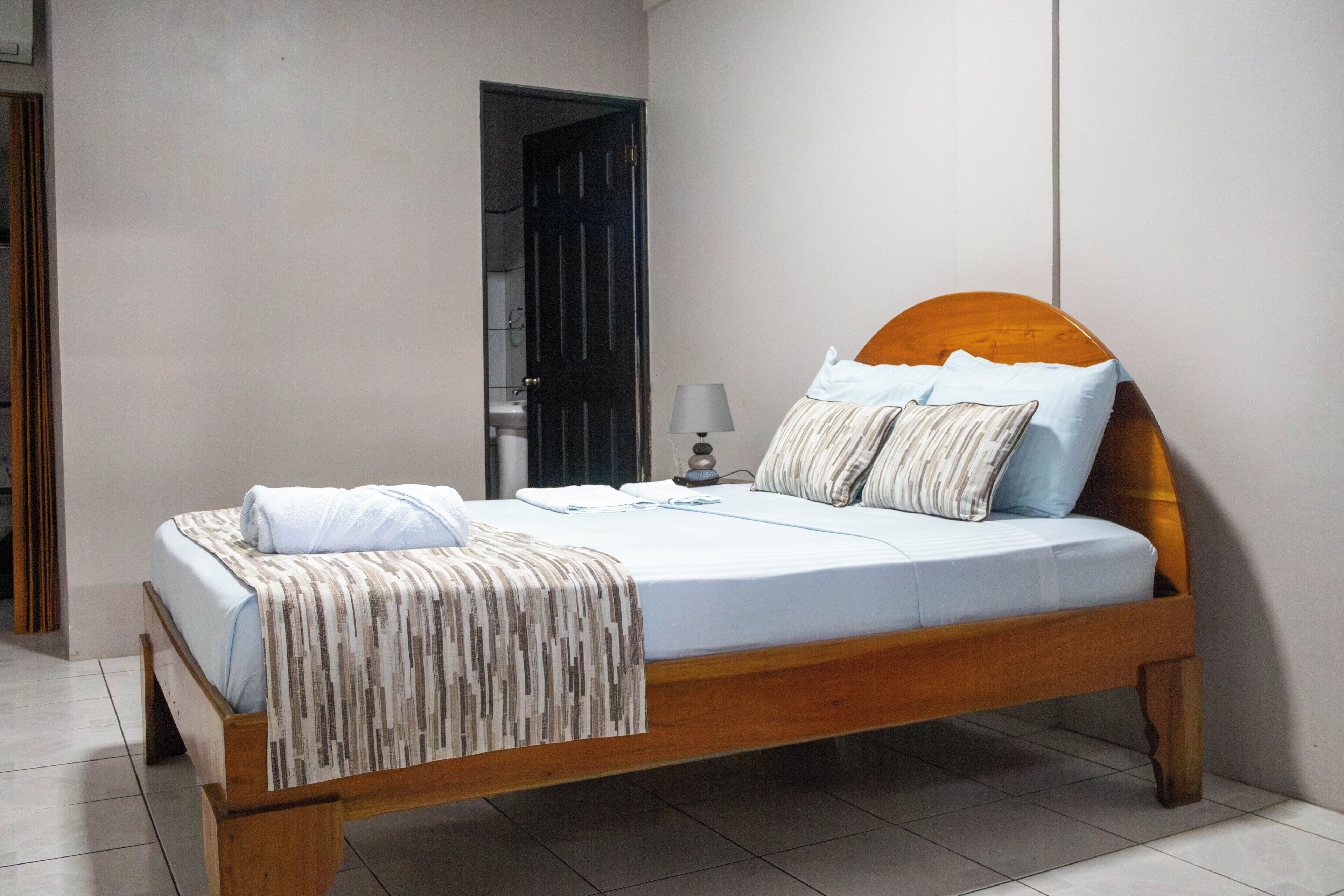 Una cama individual con cabecera de madera, ropa de cama blanca y una manta a rayas.